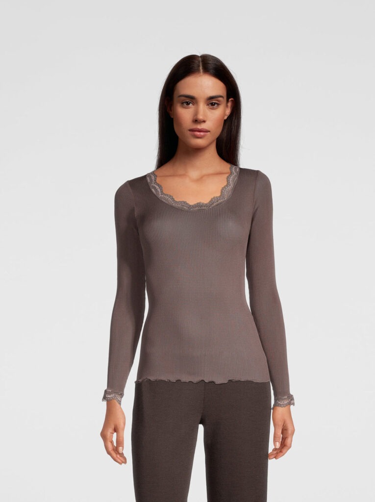 Woman wearing a taupe ribbed knit long-sleeve top with scalloped lace trim at the neckline and cuffs.