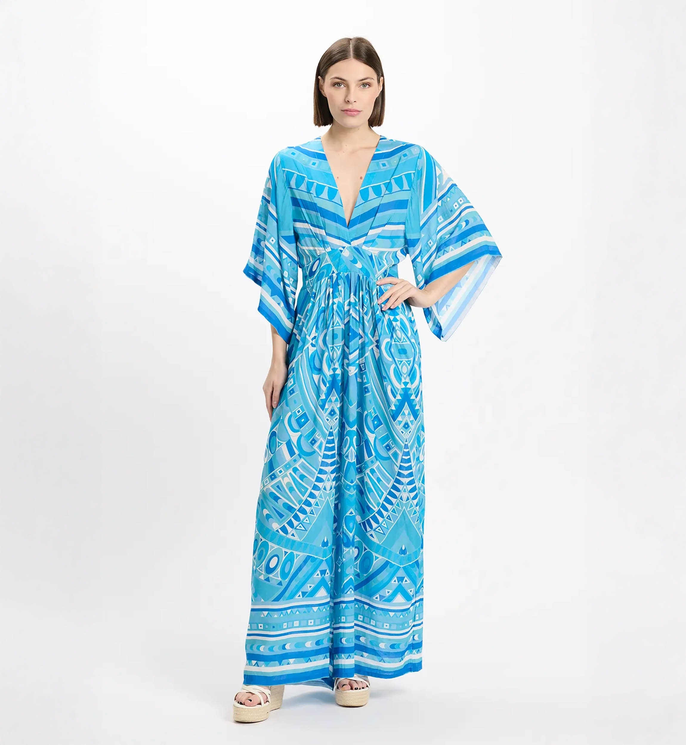 Model wearing a blue geometric print maxi dress with a plunging V-neck, wide kimono sleeves, and a tied waist, paired with espadrille sandals.
