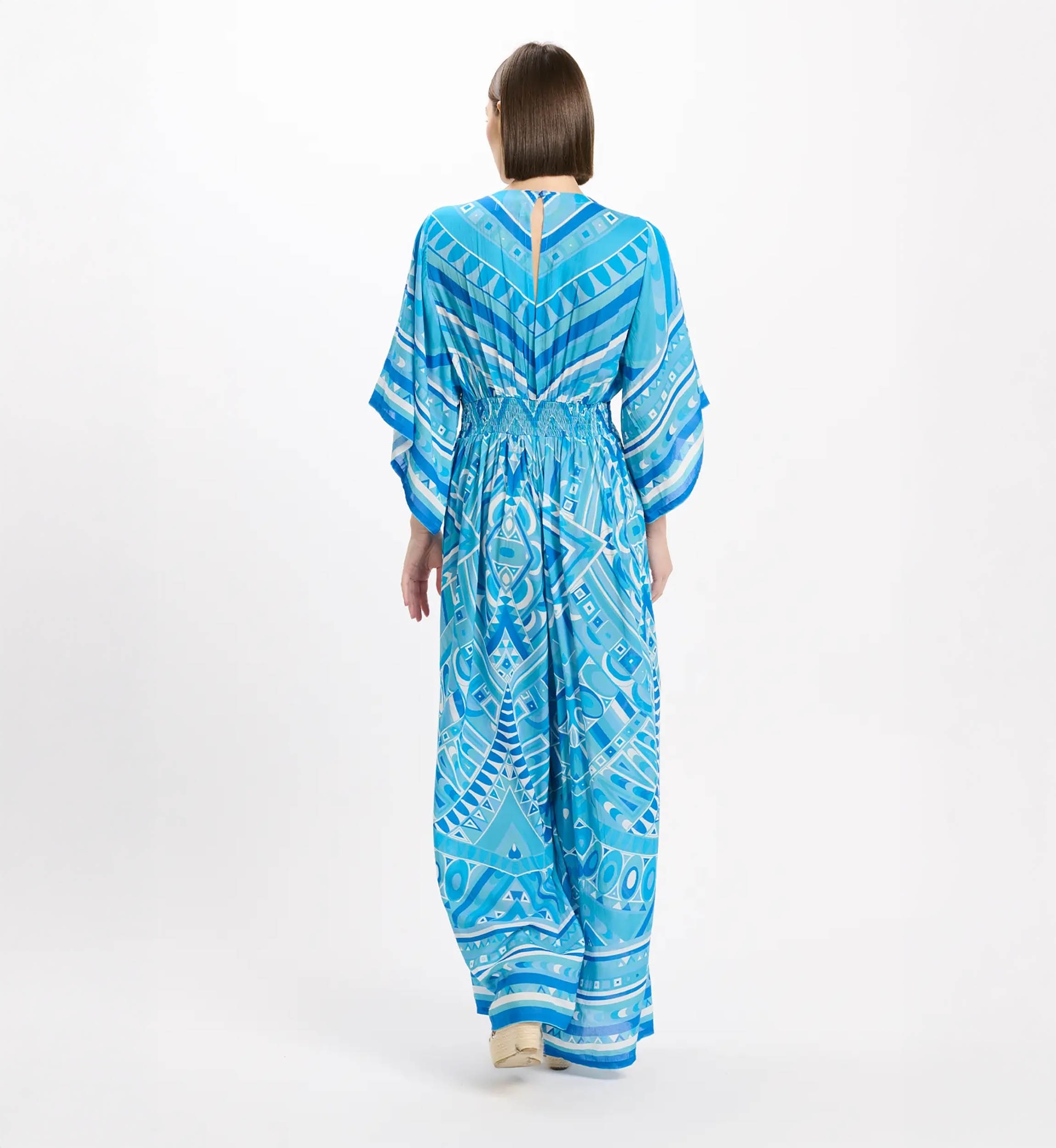 Back view of a person wearing a blue geometric print maxi dress with kimono-style sleeves and an elastic waist, standing against a white backdrop.