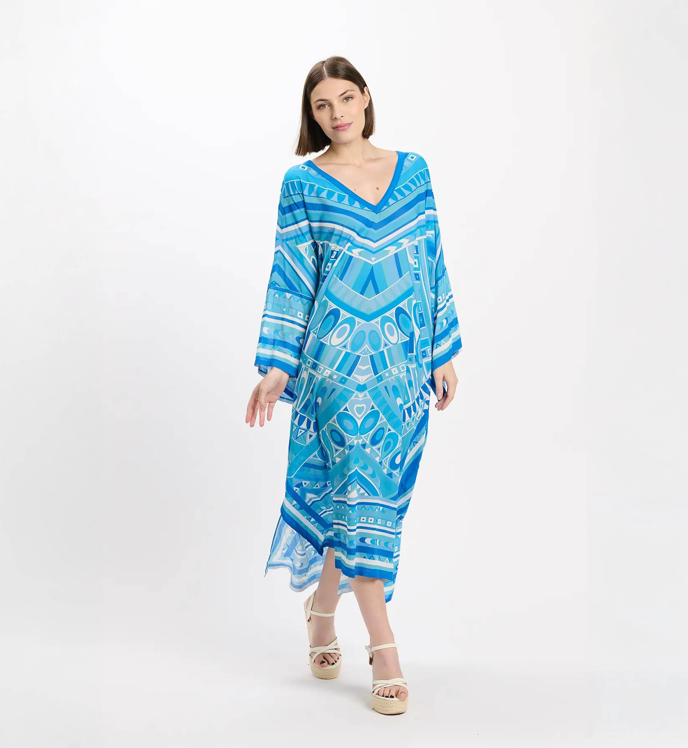 Woman in a blue geometric-printed maxi dress with long sleeves, standing against a white background.