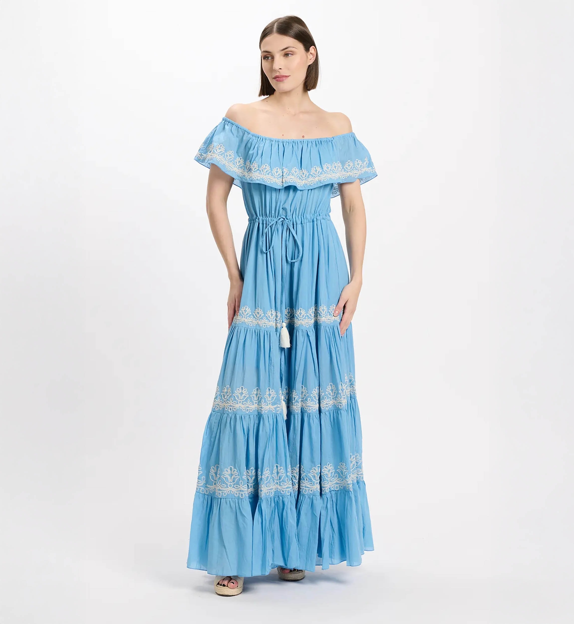 Off-shoulder blue maxi dress with white lace embroidery, cinched waist, and tiered ruffled skirt worn by a model.