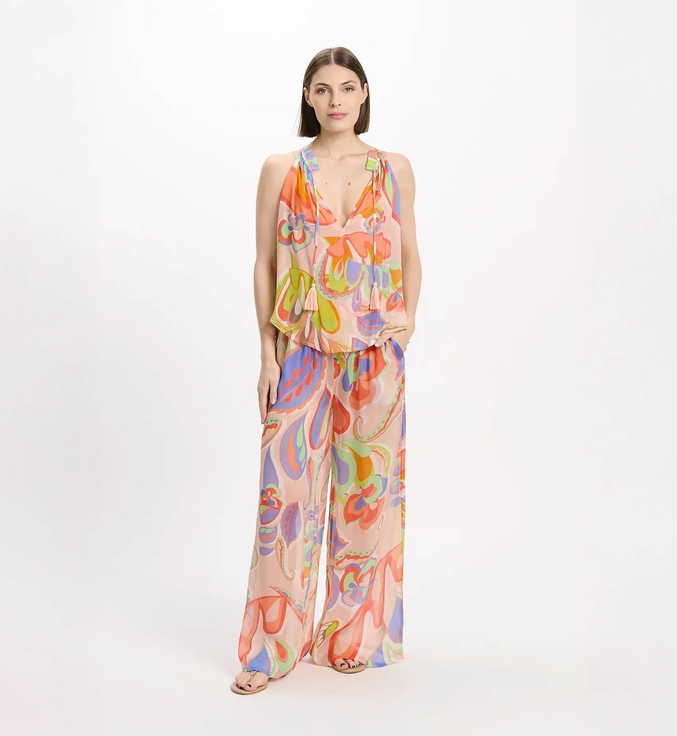 Woman wearing a multicolor abstract‑print sleeveless jumpsuit with a plunging neckline and wide-leg pants, standing against a white background.