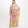 Model wearing a flowing pastel pink maxi kaftan with a vibrant abstract pattern and a jeweled belt at the waist.