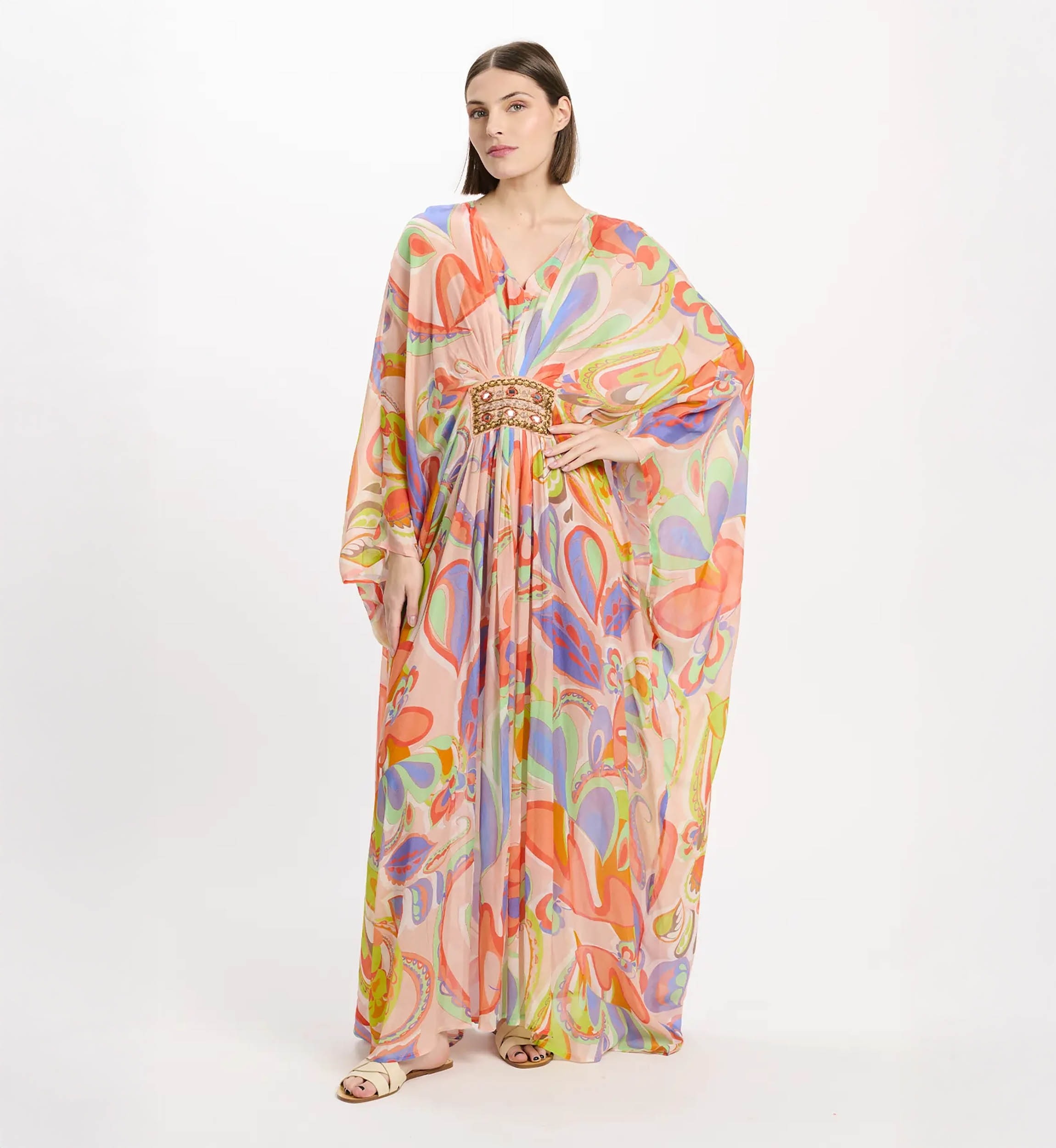 Model wearing a flowing pastel pink maxi kaftan with a vibrant abstract pattern and a jeweled belt at the waist.