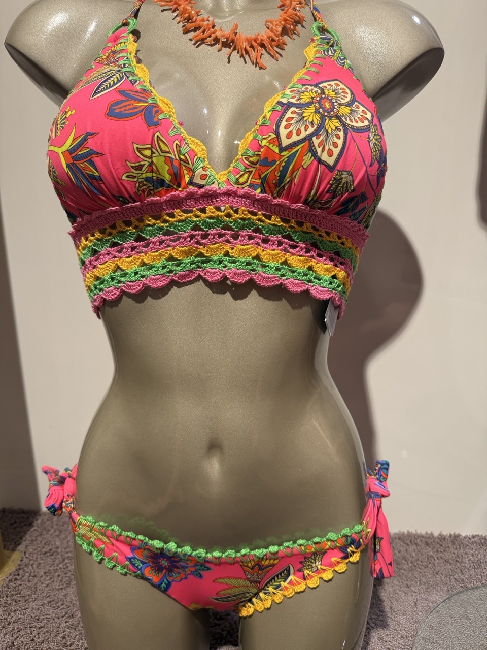 Bright pink floral bikini with multicolored crochet trim on top and bottom, displayed on a mannequin.