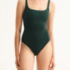 Model wearing a dark green one-piece swimsuit with a square neckline and wide straps against a light background.