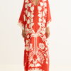 Woman wearing a flowing red kaftan with a bold white botanical print and a deep V-neck, standing barefoot.