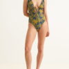 Woman wearing a navy blue one-piece swimsuit with yellow palm leaf print and a plunging front with ties at the bust.