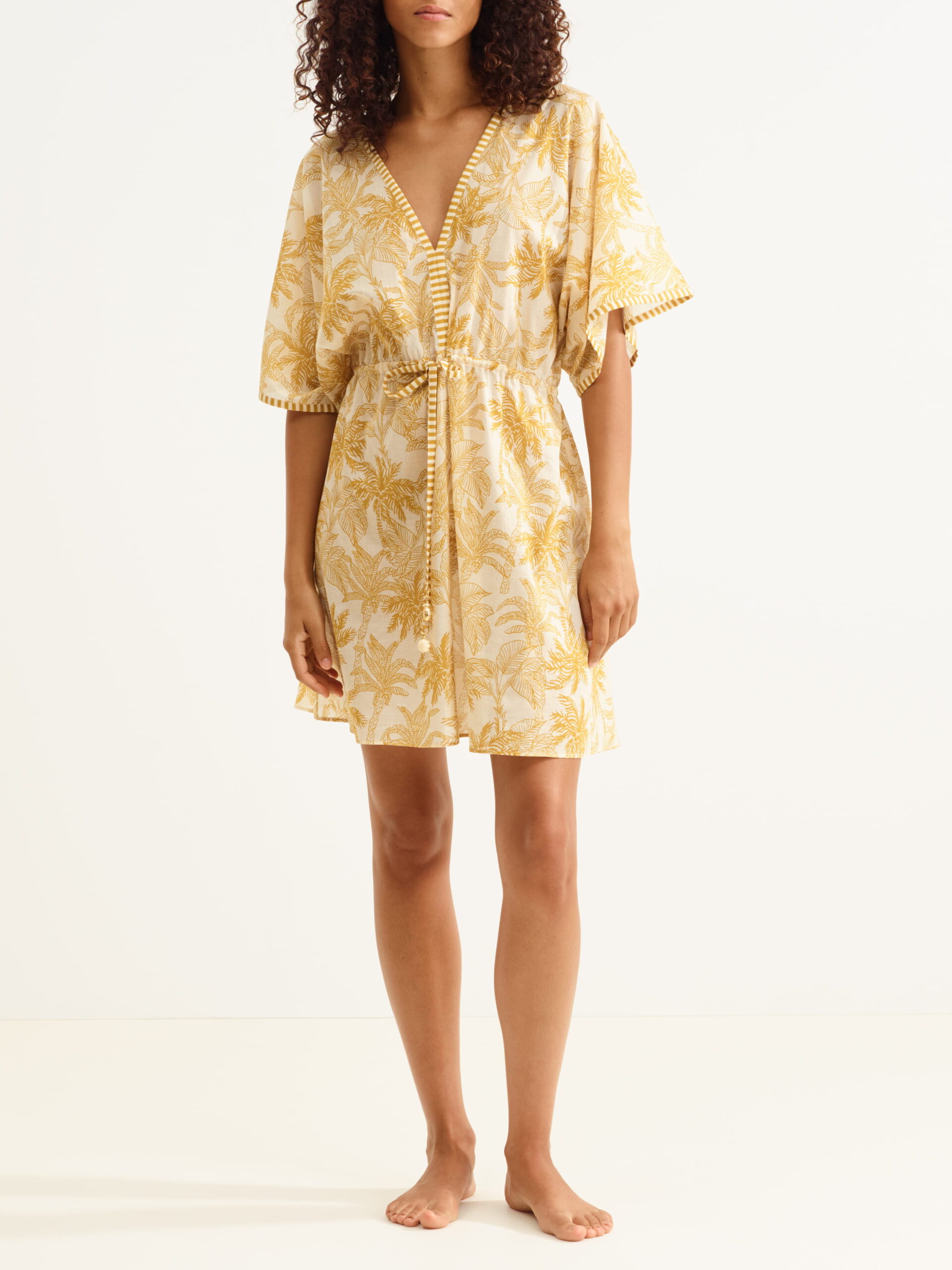 Beige kimono-style dress with yellow palm leaf print, V-neck and waist tie, worn by a barefoot model.”] ,