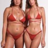 Two women wearing red bikinis stand side by side and face the camera in a studio setting with a light gray background.