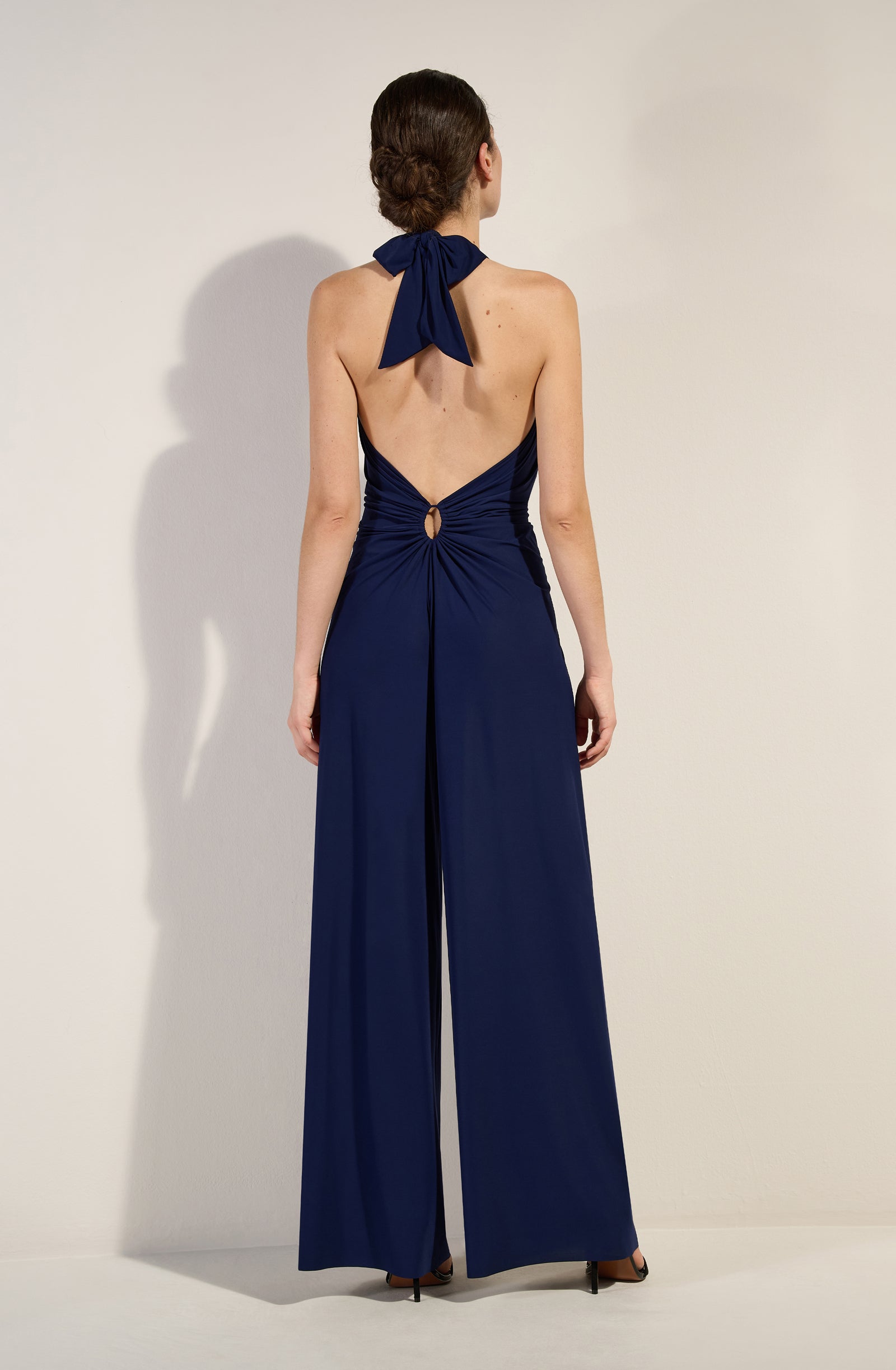 Back view of a woman in a navy halter-neck dress, with a knotted tie at the nape and a small circular back cutout.