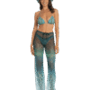 Model wearing turquoise bikini top and sheer gradient pants with a hat, smiling at the camera.