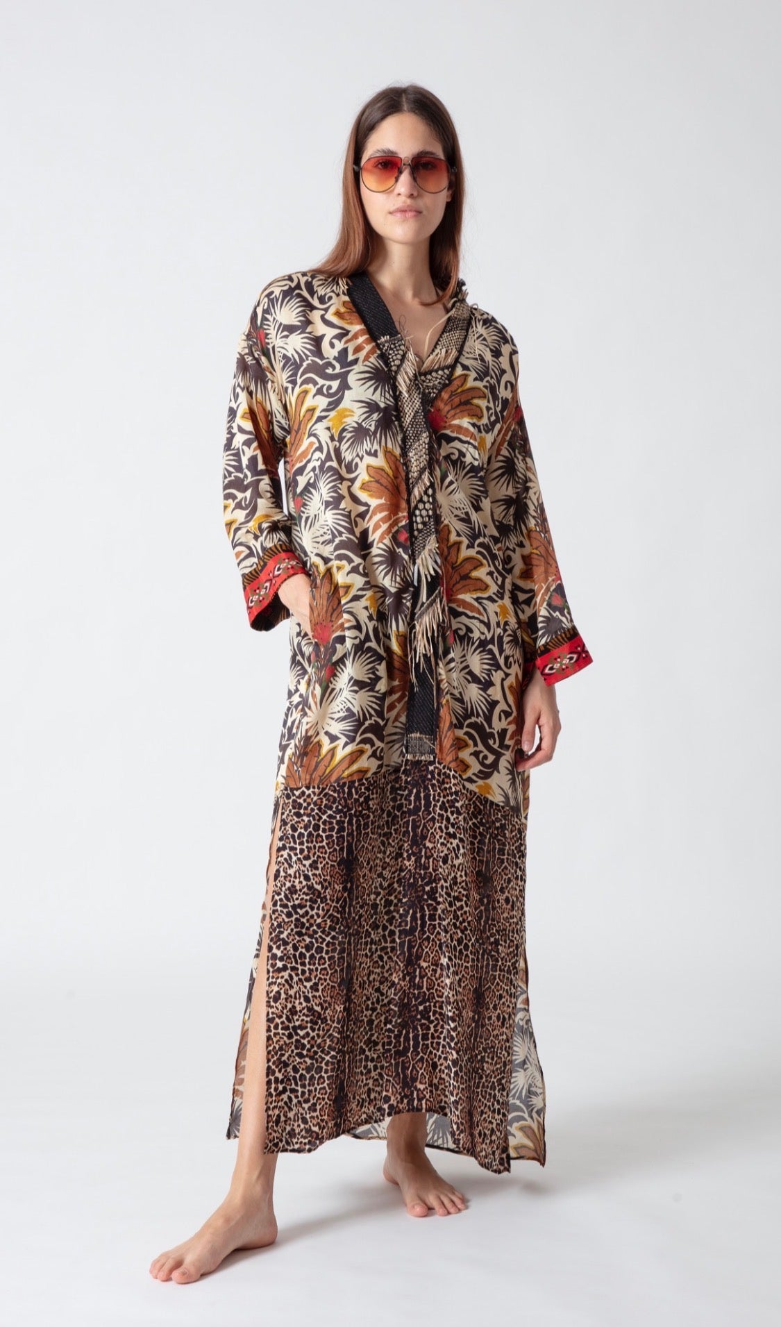 Model wearing a long, flowing maxi dress with tropical palm and leopard print patterns, plus red sunglasses.