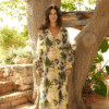 Woman stands under a large tree in a tropical-print, long-sleeve maxi dress with palm leaf patterns and sandals.