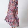 Woman wearing a blue floral maxi dress with pink blossoms, gathered waist, and flowing skirt, standing barefoot on white background.