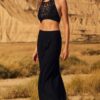 Woman in a black crochet halter top and long skirt walking across a sandy desert with cliffs in the background.