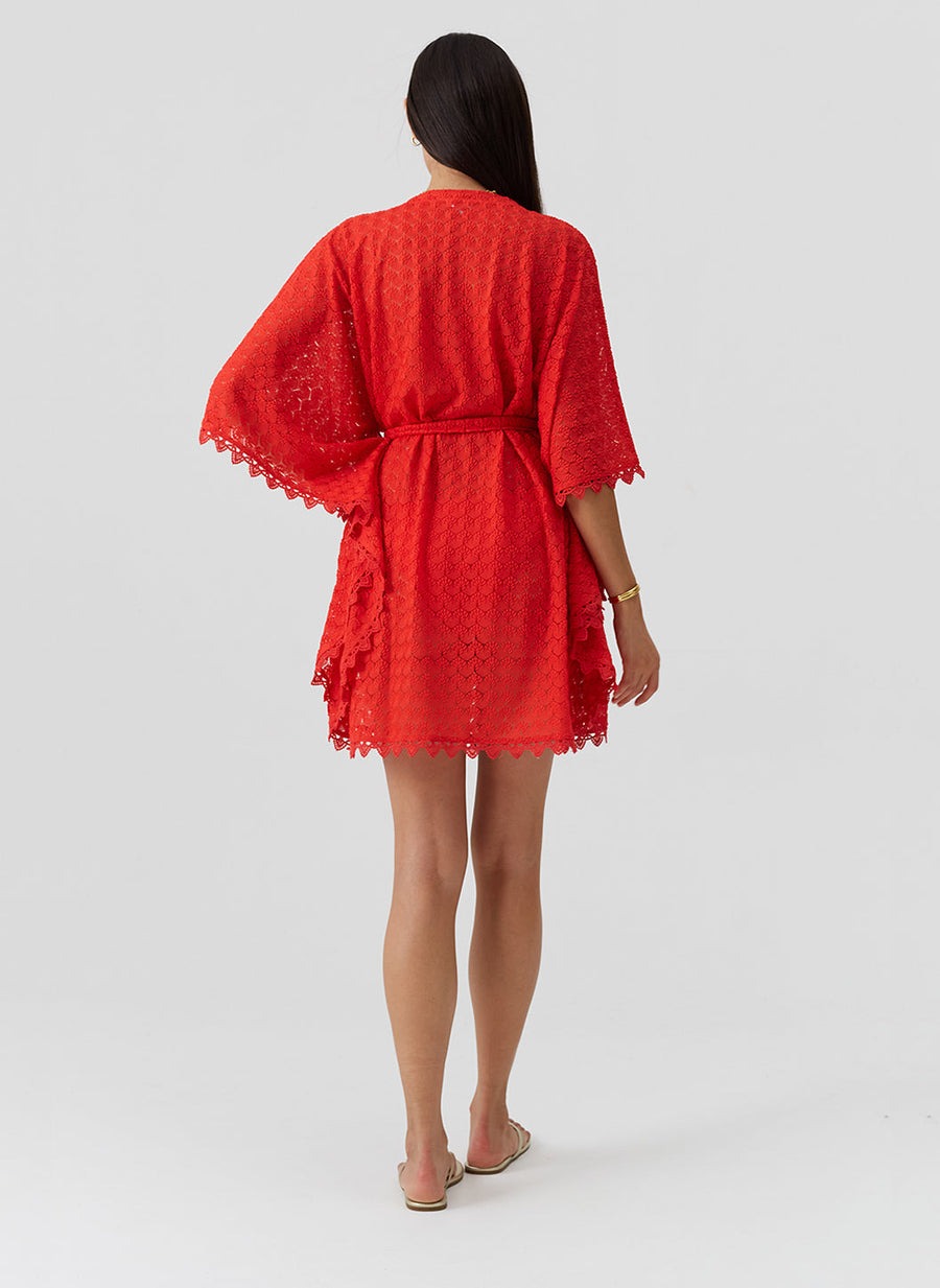 Back view of a woman in a red lace kimono-style dress with a belt and scalloped hem.",