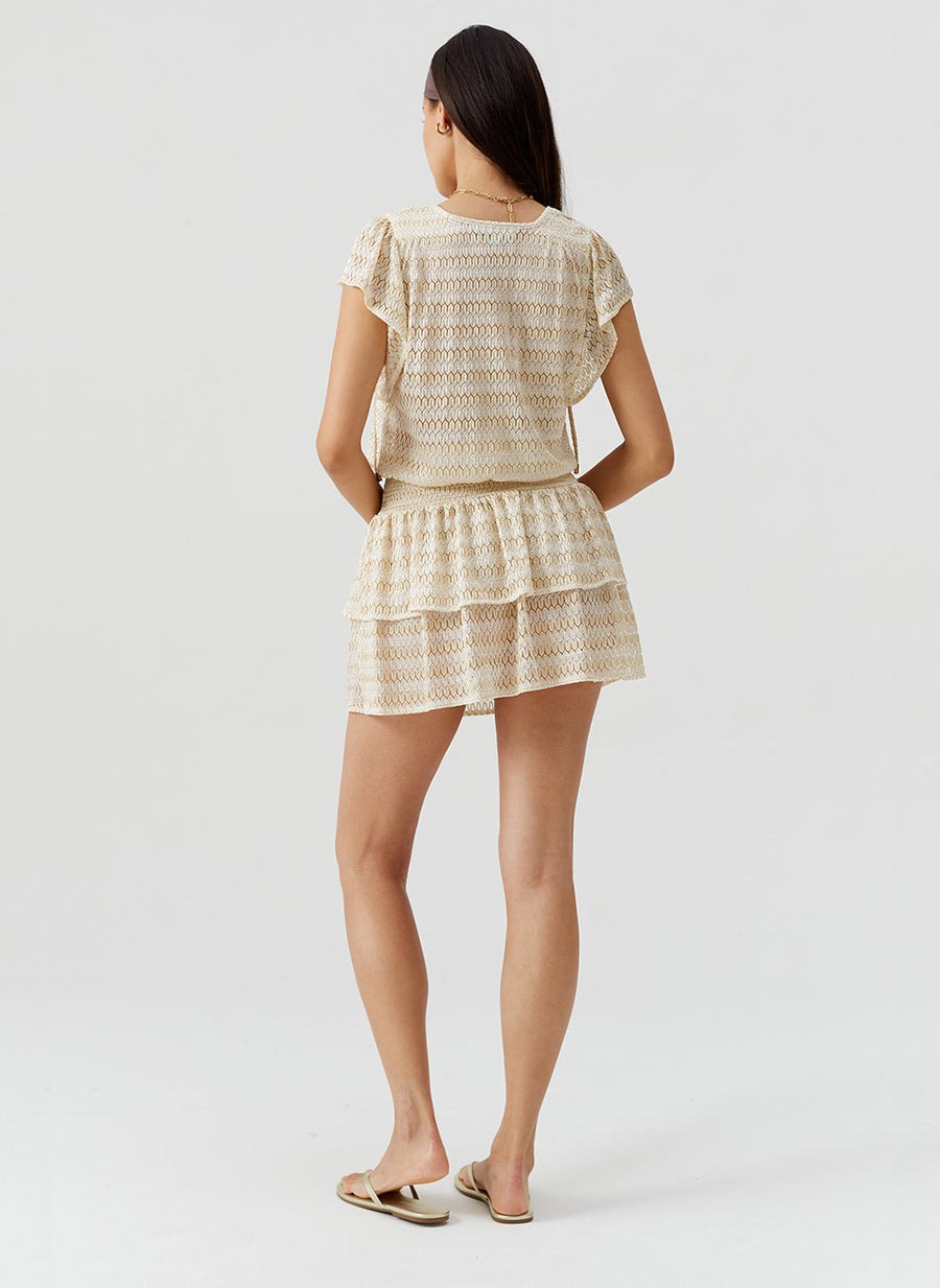 Back view of a woman wearing a cream lace short-sleeve top and matching layered shorts with flat sandals.