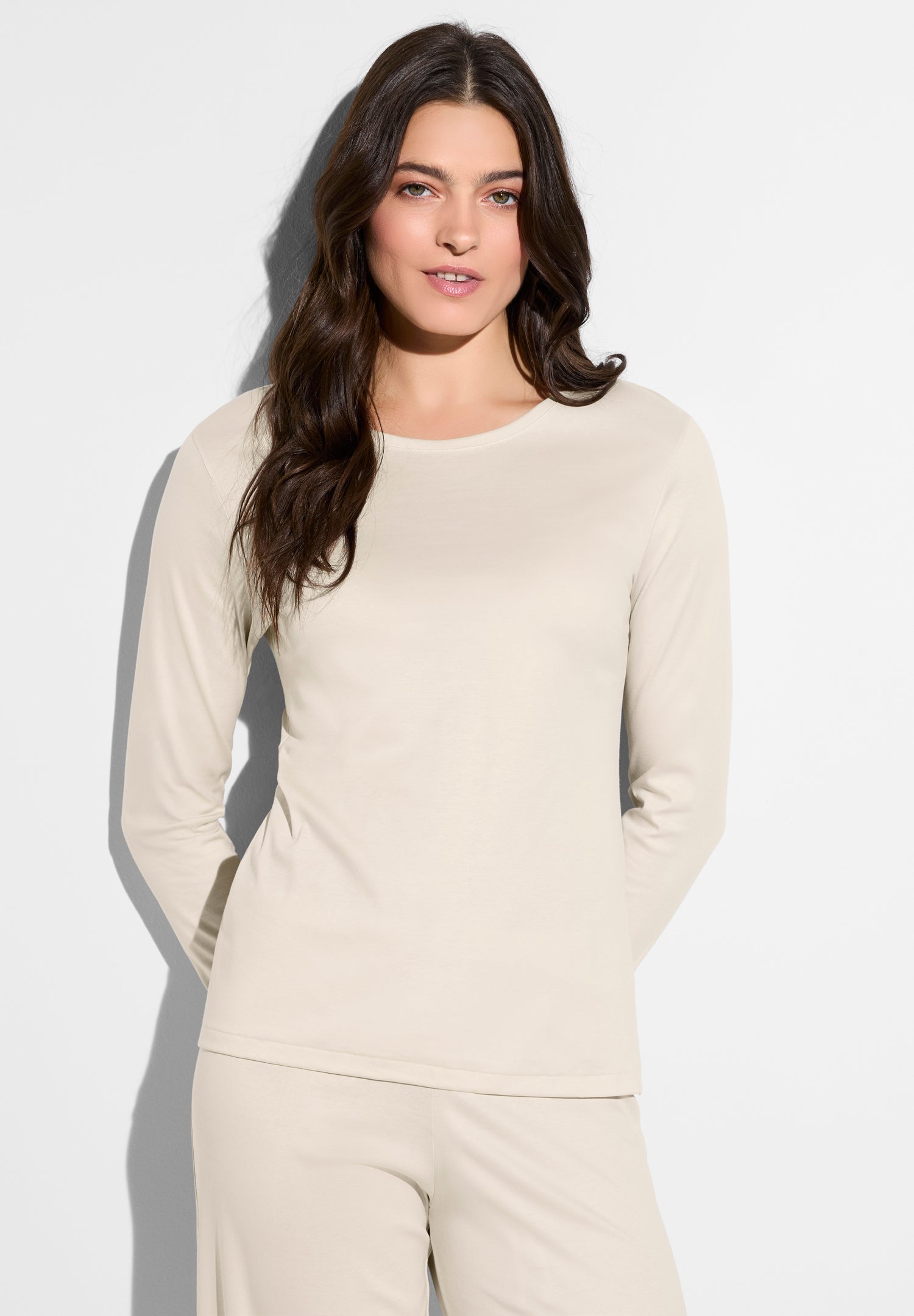 Woman with long dark hair wearing a beige top and matching pants, posing against a white backdrop.