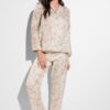 Smiling woman wearing pale pink floral pajama set, standing barefoot against a white background.