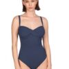Model wearing a navy blue one-piece swimsuit with twisted front detailing, standing against a white background.