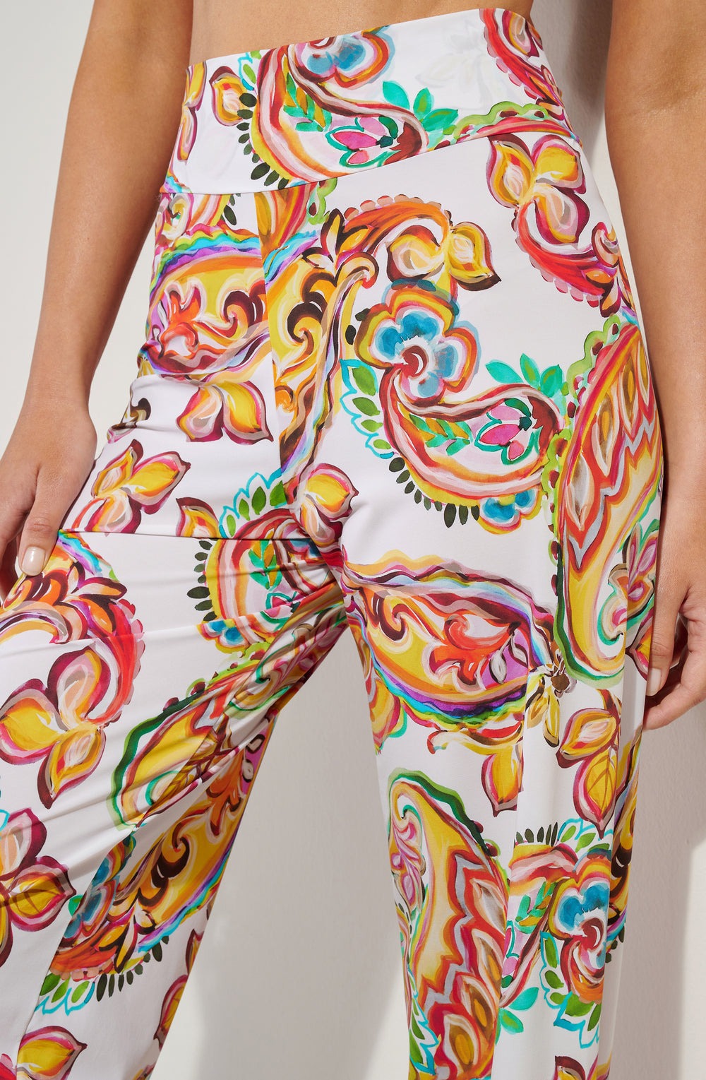 High-waisted white pants with a vibrant multicolored floral scroll print (close-up).
