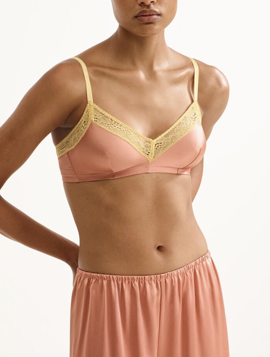 Woman modeling a peach satin bra with gold lace trim and a matching peach skirt, shown from mid-torso up against a light background.