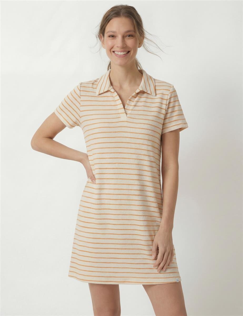 Smiling woman wearing a beige and white striped short-sleeve polo dress, standing with one hand on hip.