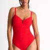 Woman wearing a bright red one-piece swimsuit with a ruched front and thin straps in a studio setting.