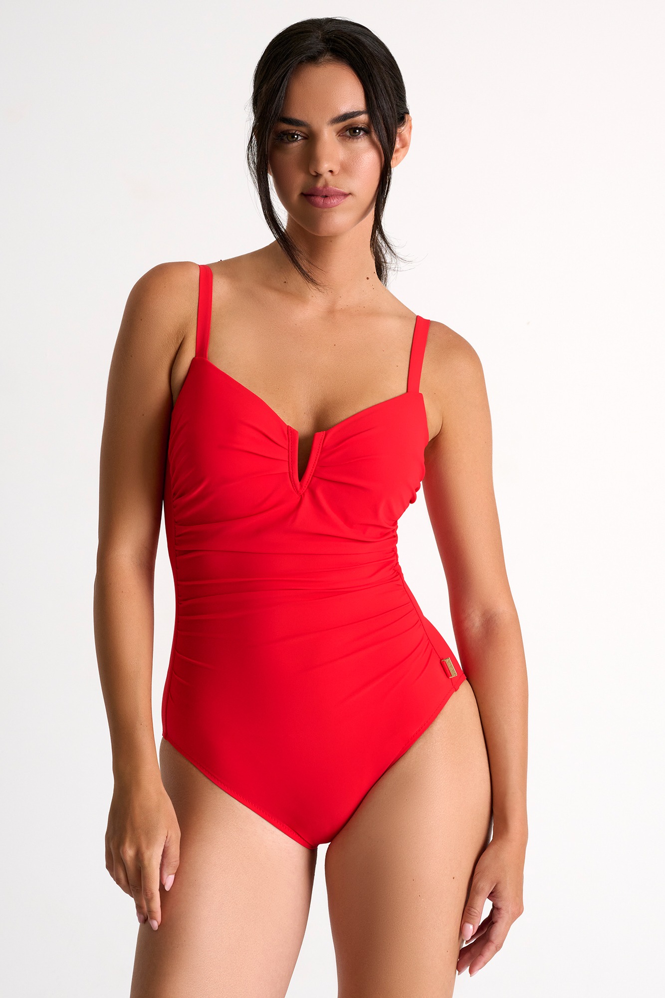 Woman wearing a bright red one-piece swimsuit with a ruched front and thin straps in a studio setting.
